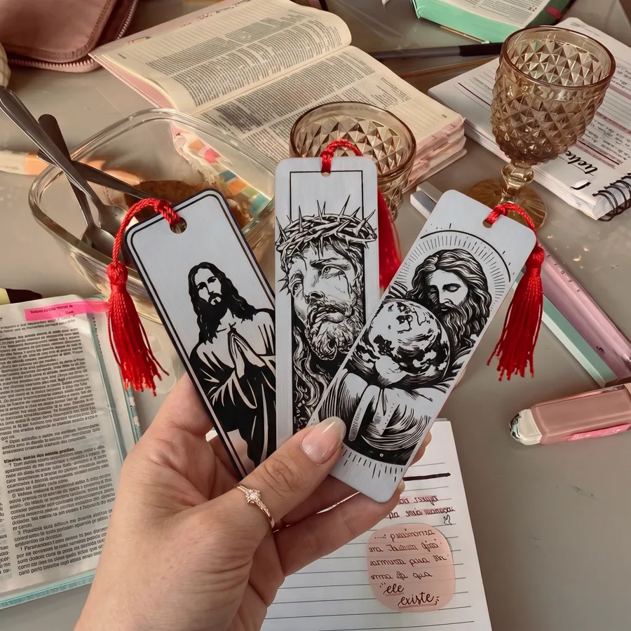 Mão segurando os 3 marcadores do kit em leque, sobre mesa de estudo com Bíblia aberta e caderno de anotações